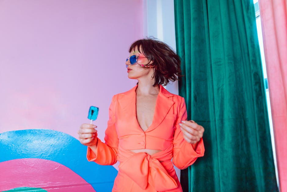 Trendy portrait featuring a woman in vibrant attire with sunglasses holding a blue lollipop.