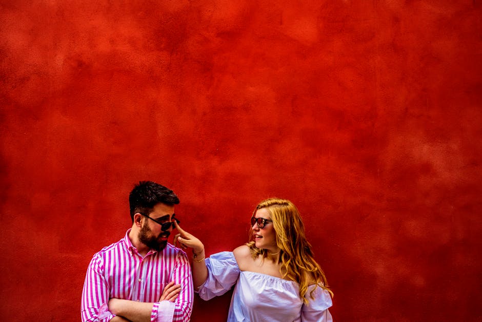 A playful couple interacts in front of a vibrant red wall in Toledo, Spain.