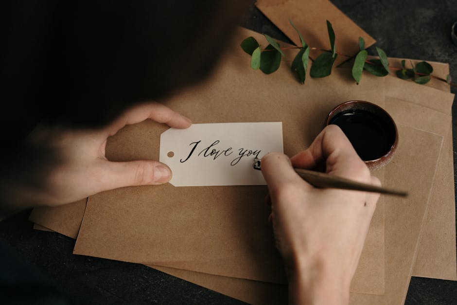 Person crafting a beautiful 'I love you' card with calligraphy, featuring eucalyptus and ink.