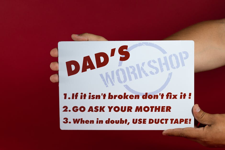 Close-up of a humorous sign with Dad's workshop rules on a red background held by hands.