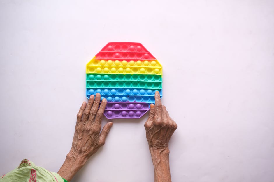Close-up of elderly hands on a rainbow silicon push popper toy on white background.