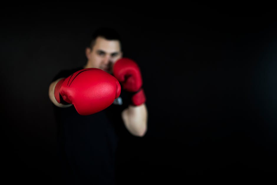 A focused boxer delivers a punch wearing bright red boxing gloves against a dark background.