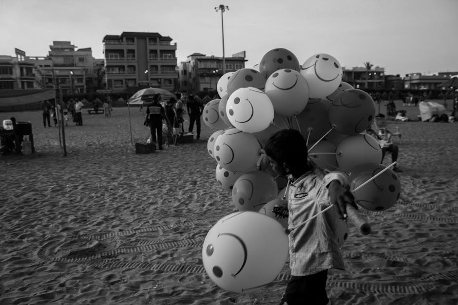 A street vendor carries smiley face balloons on a lively beach in India, capturing a vibrant scene.