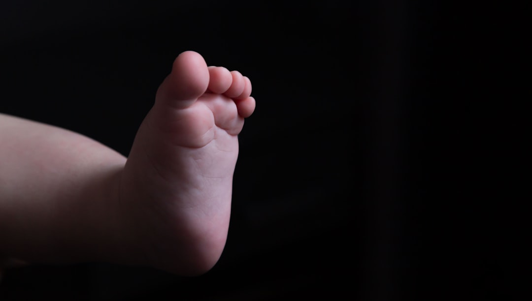 Leg of a light-skinned baby on a black background. Place for an inscription. Abortion. Motherhood. Part of the body. The close plan. Advertising. Maternity hospital. Birth. Baby. Adoption.