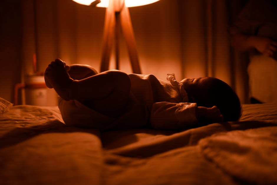 A tranquil scene of a baby sleeping on a bed, softly illuminated by a warm lamp.