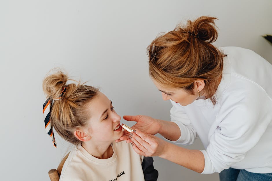 A mother bonding with her daughter by applying lipstick in a cozy indoor setting.