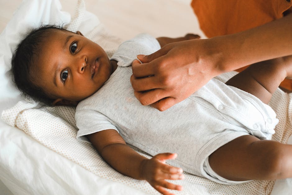 Close-up of a mother dressing her baby in a light onesie indoors.