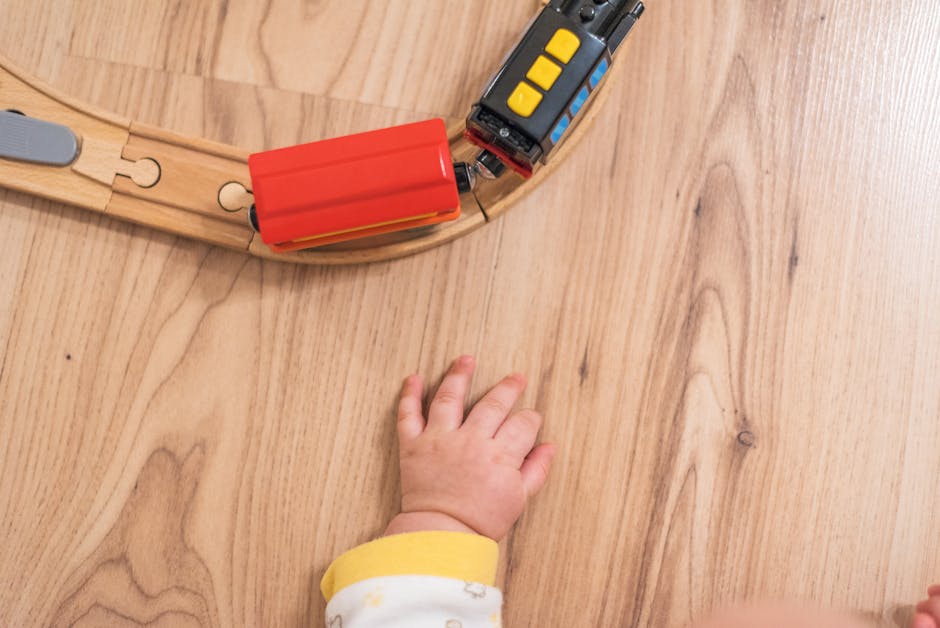 Baby hand reaching for a colorful wooden toy train on a parquet floor, fostering play and exploration. (Photo: Lukas) Baby hand reaching for a colorful wooden toy train on a parquet floor, fostering play and exploration.