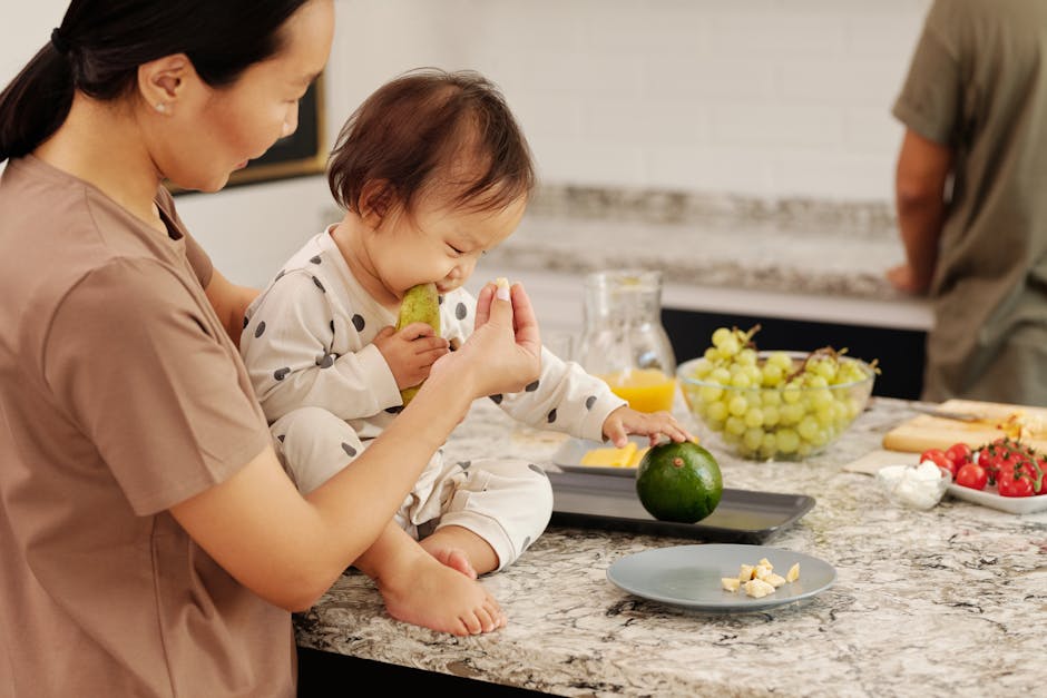 An Asian mother and her baby enjoy fresh fruit on a kitchen countertop, capturing a loving family moment.