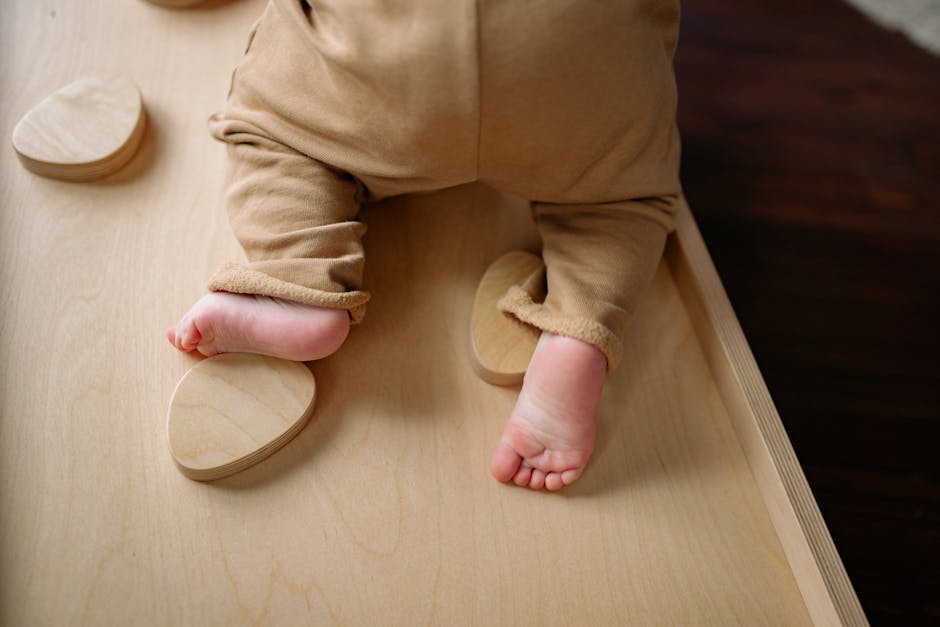 Close-up of a baby wearing an onesie climbing on indoor wooden play equipment.