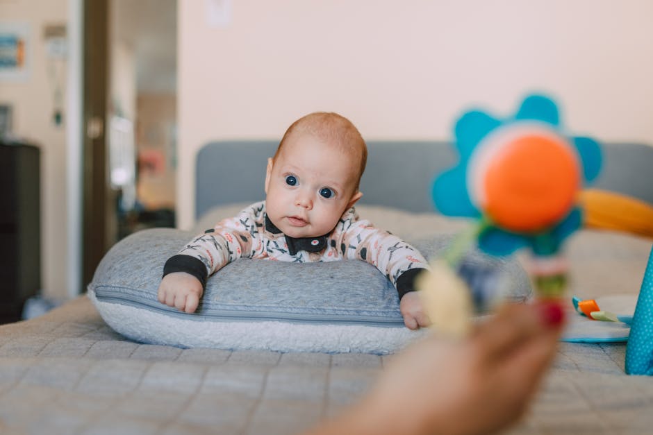 Cute baby on a bed pillow gazing at a colorful toy indoors.