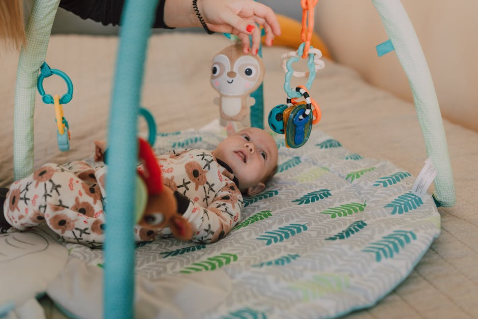 Cute baby lying on a play mat wearing a onesie and interacting with hanging toys.