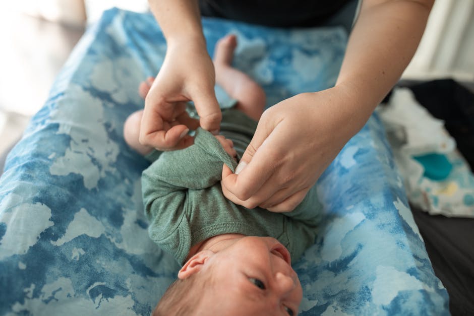 Close-up of a baby being dressed in green clothes on a blue changing table indoors.