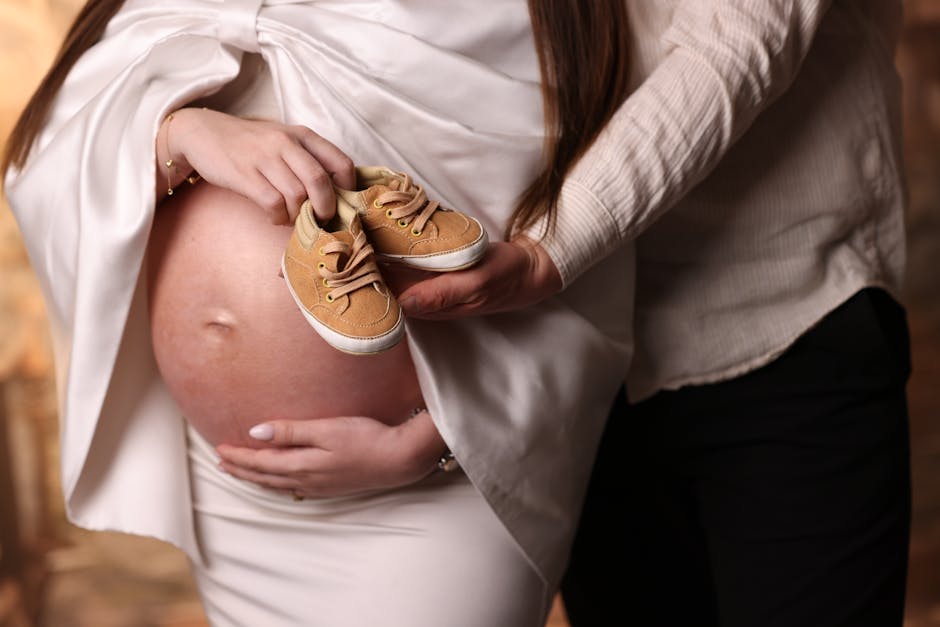 A close-up of parents holding baby shoes on a pregnant belly, symbolizing anticipation and love.