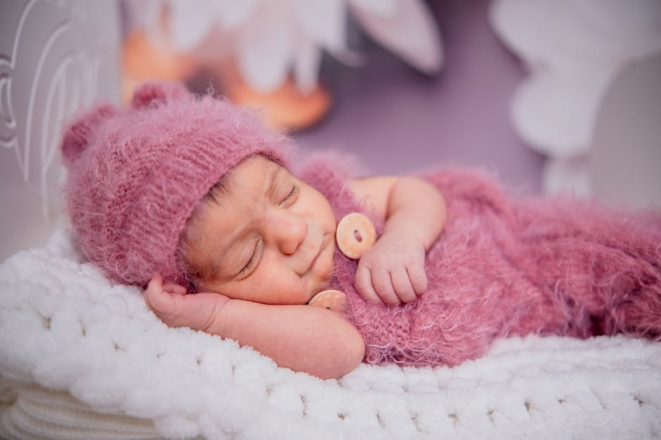 Sweet baby peacefully sleeping in pink knitted outfit on soft white blanket.
