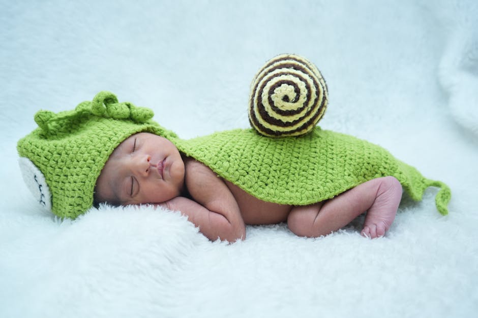 Adorable newborn baby sleeping in a green knitted snail costume on a soft white blanket.