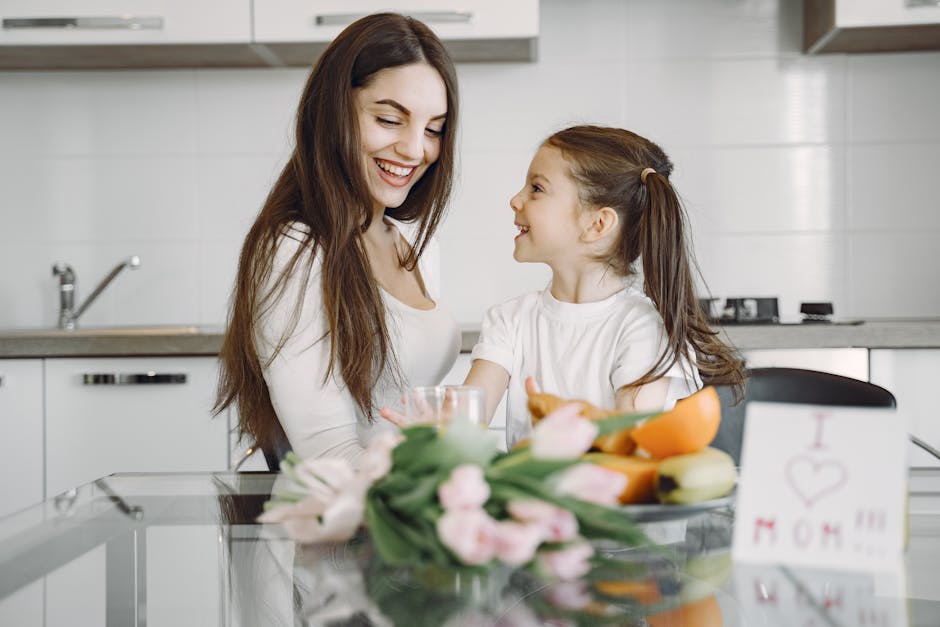 A cheerful mother and daughter share a joyful moment in a bright, modern kitchen with flowers and fruits. (Photo: Gustavo Fring) A cheerful mother and daughter share a joyful moment in a bright, modern kitchen with flowers and fruits.