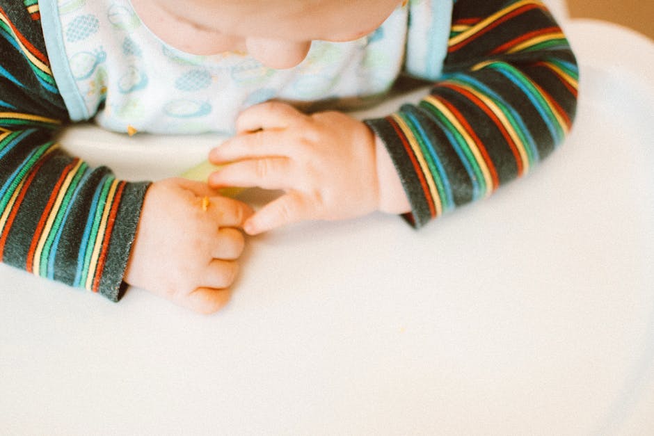 Adorable baby playing with food on a high chair indoors, highlighting innocence and curiosity.