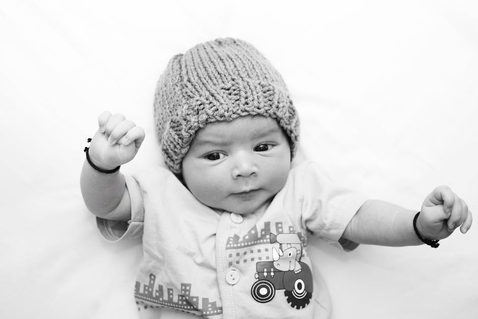 Adorable baby wearing a knitted hat, lying on a white surface, with a playful expression.