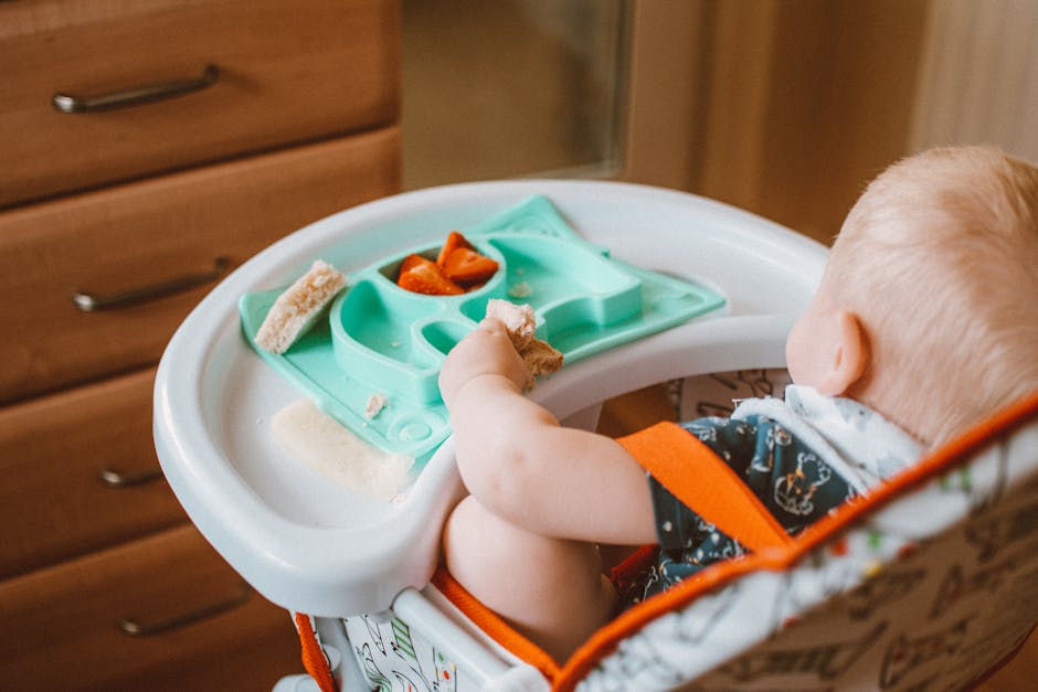 A cute baby enjoying snack time in a high chair with colorful food tray indoors.