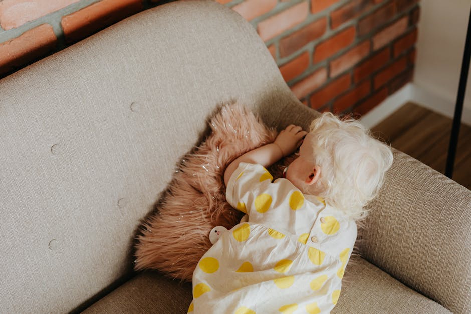 Adorable toddler sleeping on a couch in a polka dot dress with white hair, capturing innocence and calm.