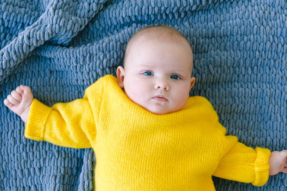 Top view of adorable baby in yellow sweater looking at camera while resting on soft blue blanket in room at daytime (Photo: Anna Shvets) Top view of adorable baby in yellow sweater looking at camera while resting on soft blue blanket in room at daytime